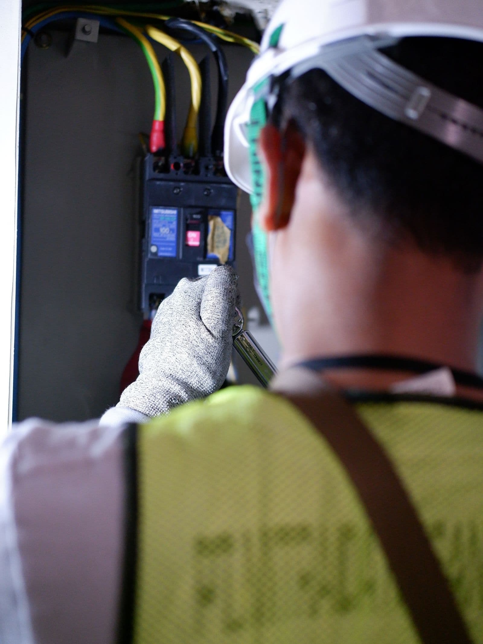 An electrician working at an open breaker panel, testing a live circuit by hand